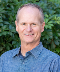 Our team member, Professional headshot of Keith Courtney, co-founder of ACI Apartments, wearing a denim shirt and smiling.